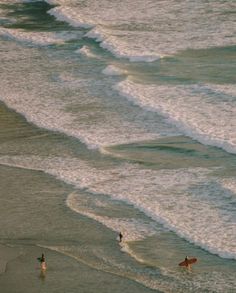 two surfers are walking into the ocean with their surfboards in front of them