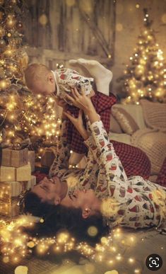 a woman holding a baby in her arms while laying on the floor next to a christmas tree