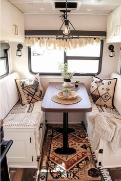 a table and bench in the back of a camper with pillows on it's sides