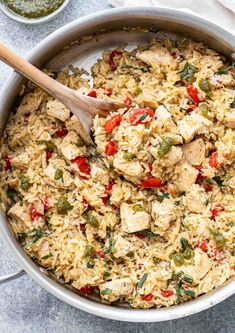 a pot filled with rice and vegetables on top of a table next to a wooden spoon