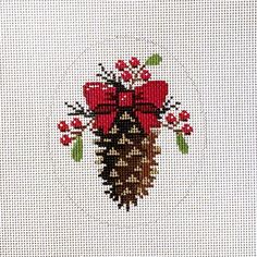 a cross - stitch christmas card with a pine cone and bow on it's side