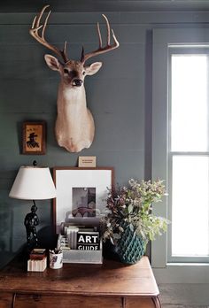 a deer head mounted on the wall next to a table with flowers and other items