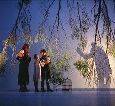 four people standing in front of a tree with branches hanging from it's branches