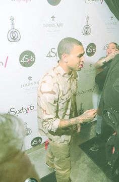 a man standing in front of a white wall talking to another man with tattoos on his arm