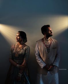 a man and woman standing next to each other in front of a wall with lights on it