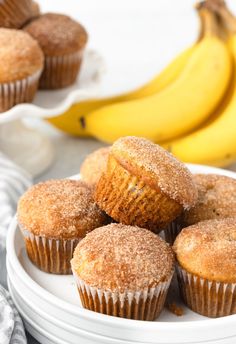 some sugary muffins on a white plate with bananas in the back ground