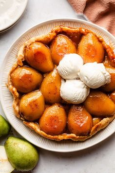 an apple pie with ice cream on top sits on a plate next to some pears