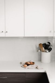 a kitchen counter with white cabinets and wooden utensils