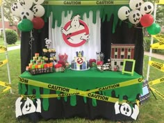 a green table topped with lots of candy and balloons in front of a sign that says caution