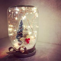 a glass jar filled with snow and christmas decorations on top of a table next to a wall