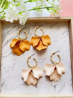 three flower shaped earrings sitting on top of a marble table next to white and pink flowers