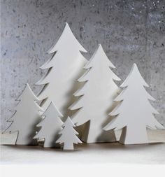 three white wooden christmas trees sitting next to each other on top of a table in front of a concrete wall