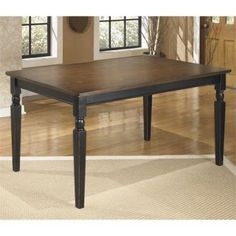 a wooden table sitting on top of a hard wood floor next to two windows in a living room