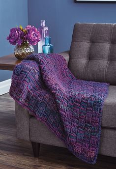 a couch with a blanket on top of it next to a table and flowers in a vase