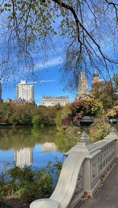 a bench sitting next to a body of water in a park with trees and buildings