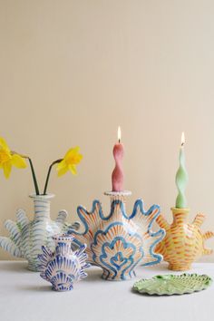 three vases with flowers in them sitting on a table next to plates and candles