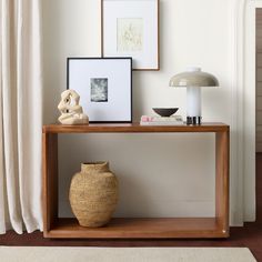 a wooden table topped with a vase next to a lamp and pictures on the wall