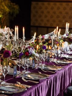 a long table is set up with purple linens and silverware for an elegant dinner