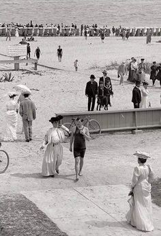 an old black and white photo of people walking on the beach with their bikes in front of them