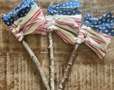 three small american flags on sticks are sitting on a wooden surface, one is red white and blue