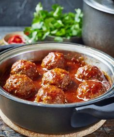 some meatballs are sitting in a pot on a wooden table next to other food