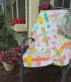 a colorful quilt on a chair in front of some potted plants and flower boxes