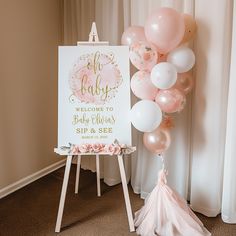 a baby shower sign with balloons in front of it and a pink tasseled pom pom