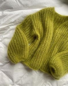 a green knitted sweater laying on top of a white bed sheet with the bottom half rolled up