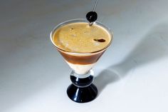 an alcoholic drink in a martini glass on a white table with a black stick sticking out of it