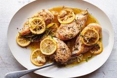 a white plate topped with chicken covered in lemons and herbs next to a fork