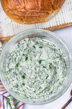 a glass bowl filled with spinach dip on top of a table next to bread