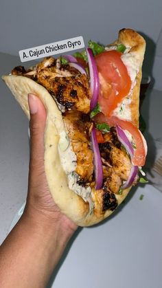 a hand holding a chicken gyro with tomatoes and onions