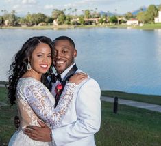 a bride and groom standing next to each other in front of a lake