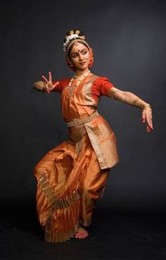 a woman in an orange and gold dress is doing a dance move with her hands