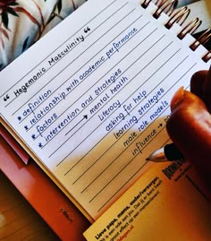 a person holding a pen and writing on a notepad next to an open notebook