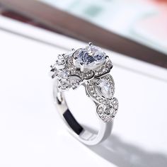 a diamond ring is shown on a white surface with other jewelry items in the background