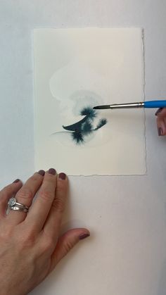 a woman is painting an image with watercolors on paper and using a brush