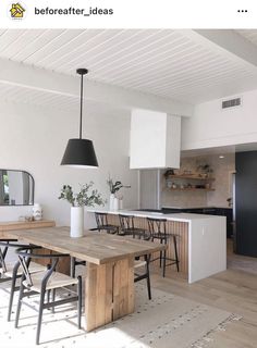 an open kitchen and dining room with white walls, wood flooring and black accents