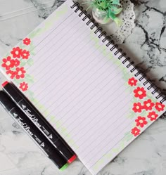 a notepad with red flowers on it next to two black pens and a succulent plant