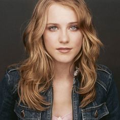 a close up of a person wearing a jean jacket and posing for a photo in front of a black background