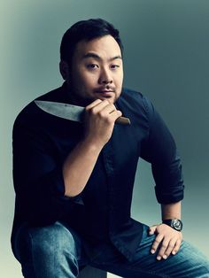 a man sitting on a stool holding a knife in his hand and looking at the camera