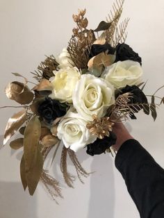 a person holding a bouquet of white and black flowers with gold leaves on the stems