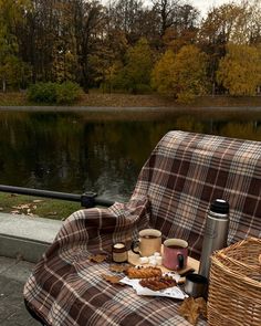 a picnic blanket with coffee cups and bread on it next to a lake in the fall