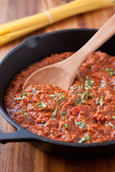 a wooden spoon in a black pot filled with chili and cheese sauce on top of a cutting board