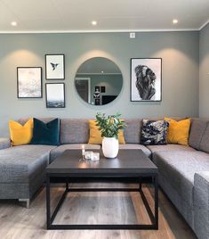 a living room with grey couches, yellow pillows and pictures on the wall above