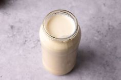 a glass jar filled with milk sitting on top of a gray counter next to an apple