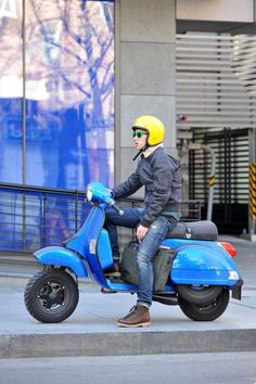 a man riding on the back of a blue scooter in front of a building