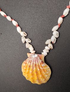 a necklace made with shells and beads on a black surface, featuring a shell in the shape of a starfish