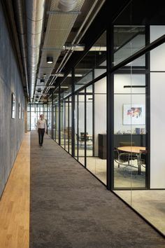 an office hallway with glass walls and wood flooring, along with a person walking down the hall