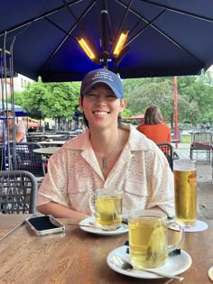 a woman sitting at a table with two beers in front of her and an umbrella over her head